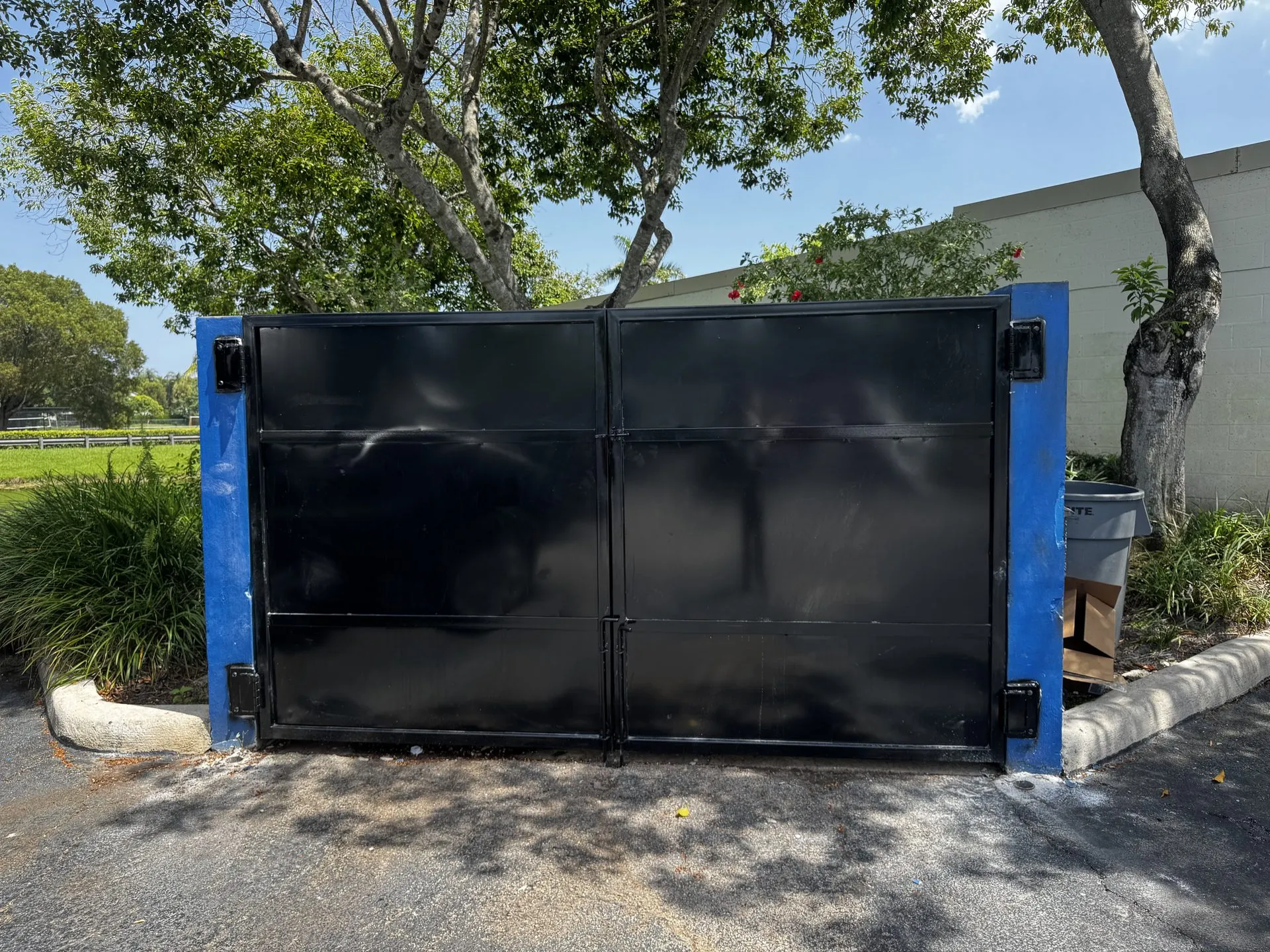 Custom black steel dumpster enclosure gates installed in a parking lot