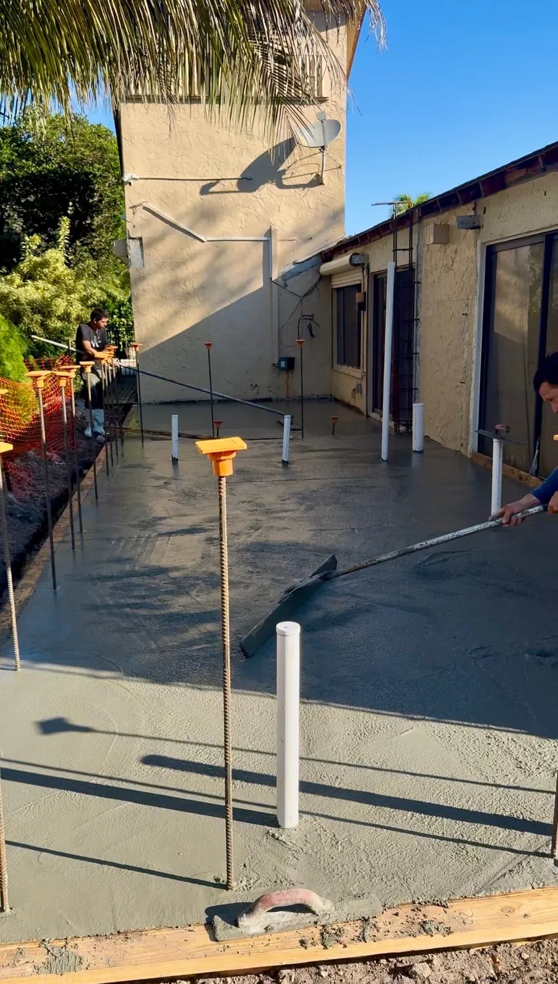 Worker screeding a fresh concrete patio slab reinforced with rebar