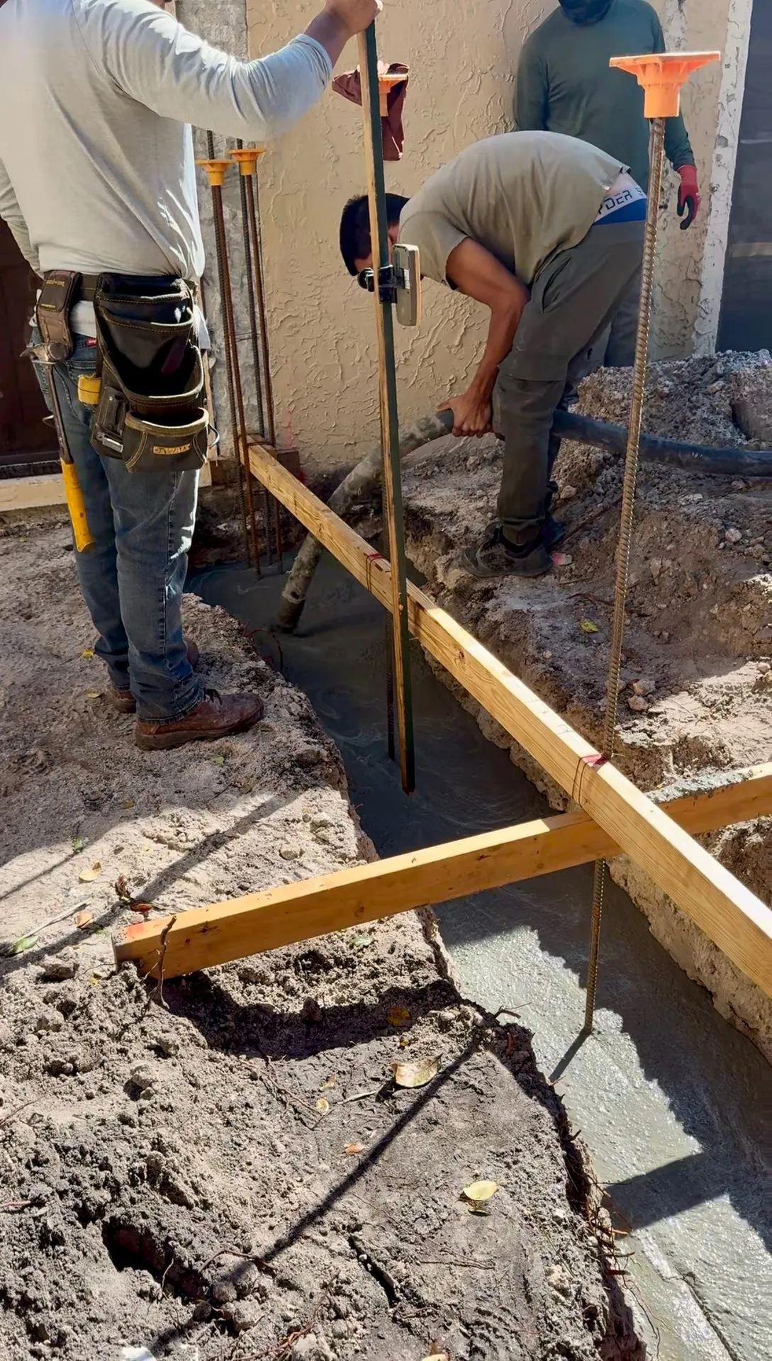Workers pouring concrete into a rebar-reinforced footing trench