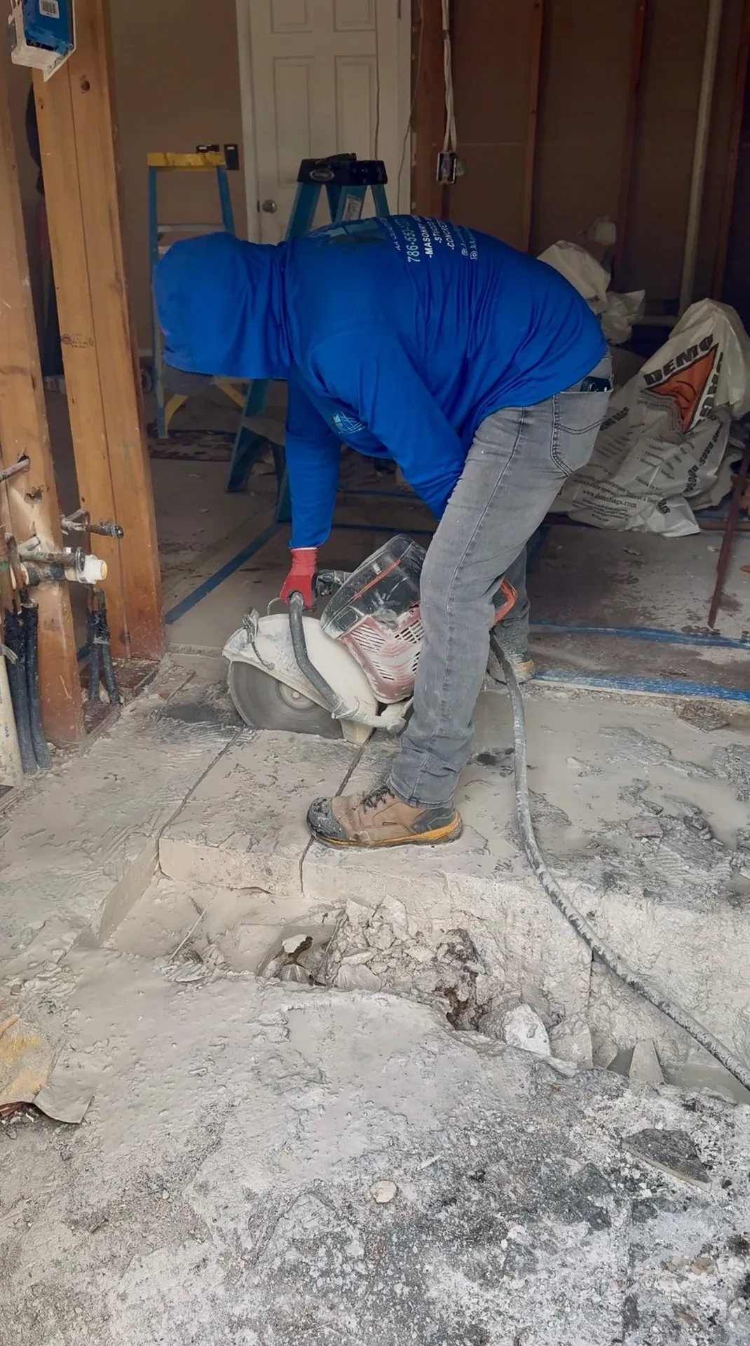 Worker saw-cutting concrete flooring inside a home renovation