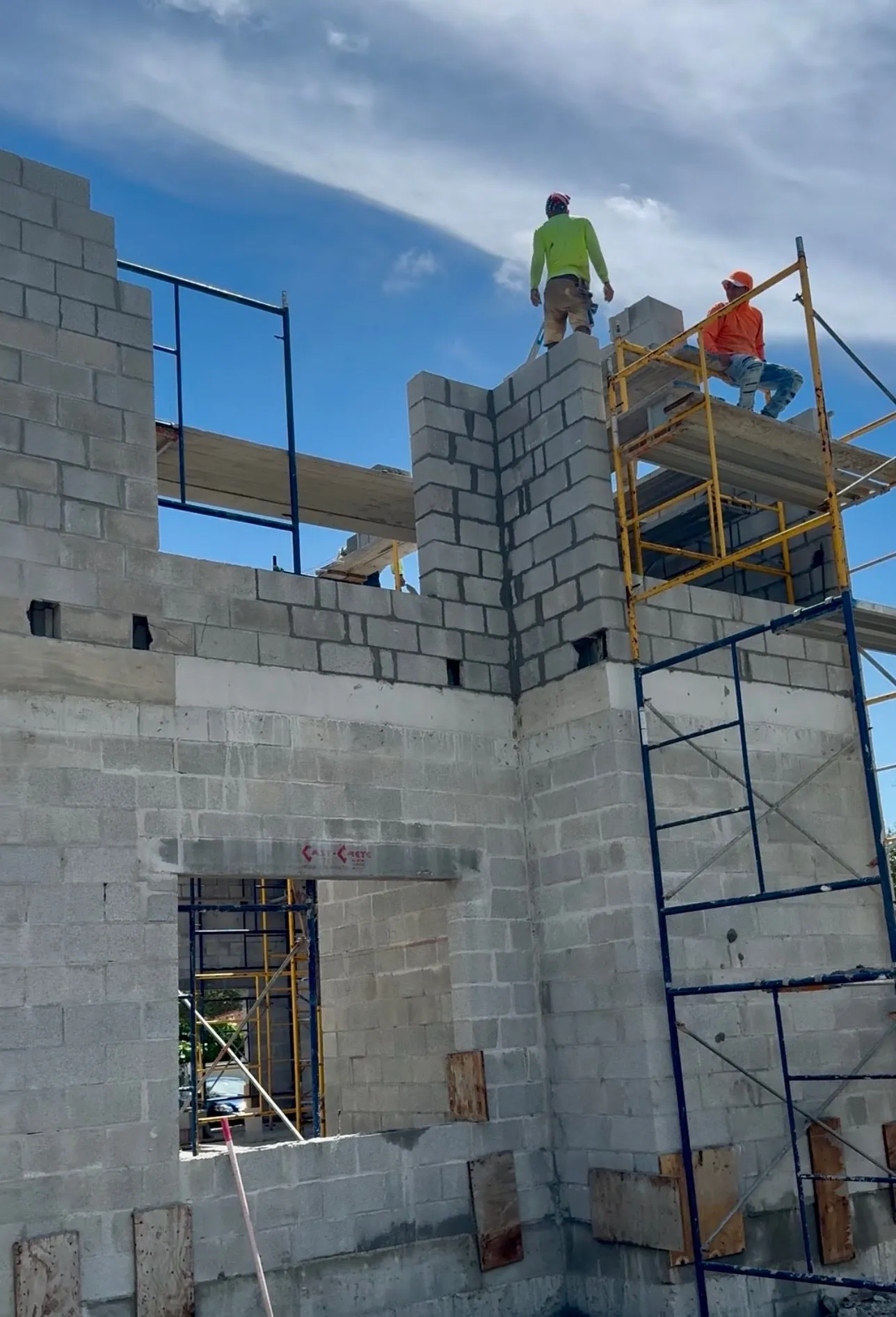 Masonry workers on scaffolding at the top of a tall concrete block structure