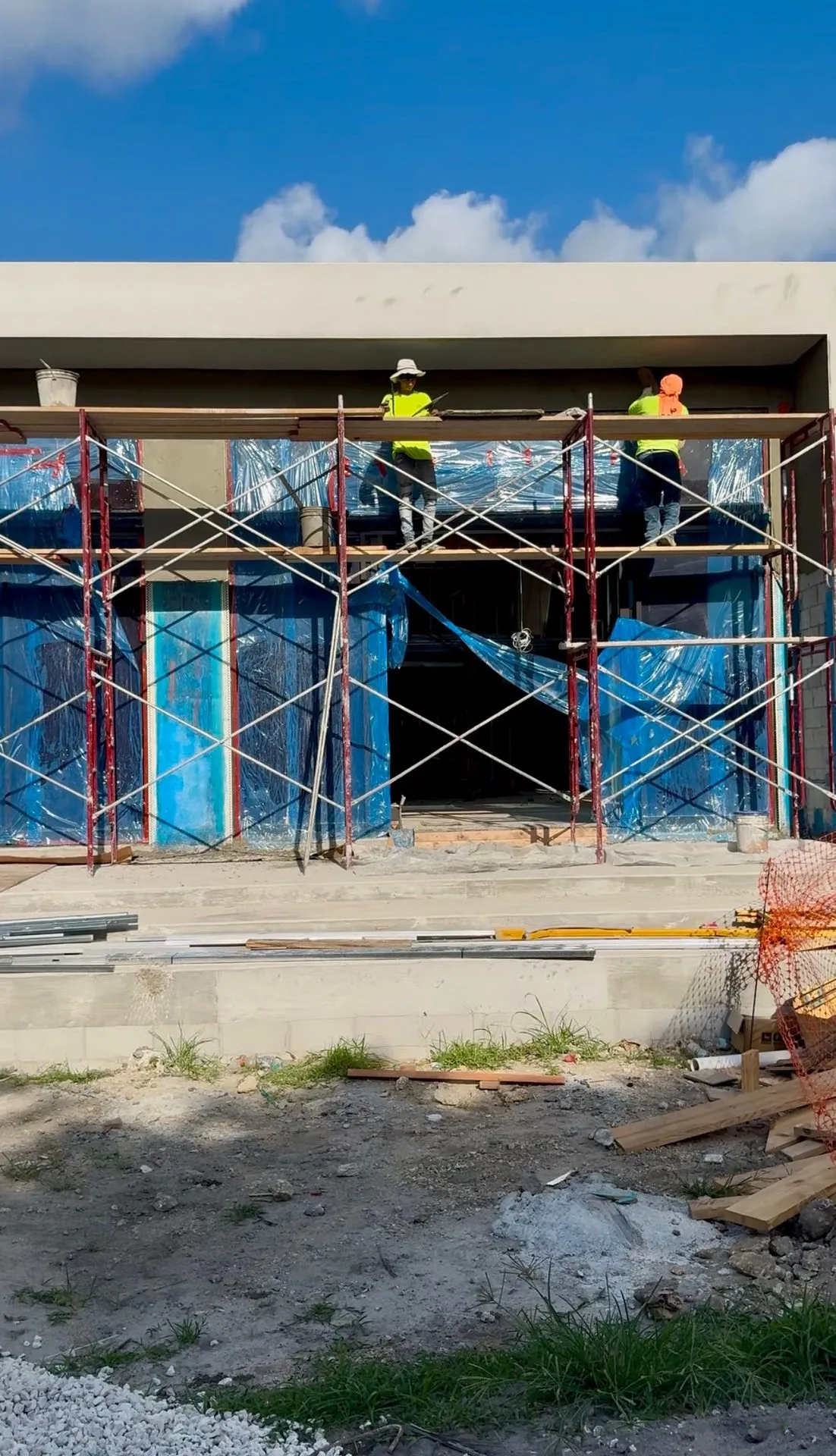 Workers on scaffolding at a block building wrapped in protective sheeting