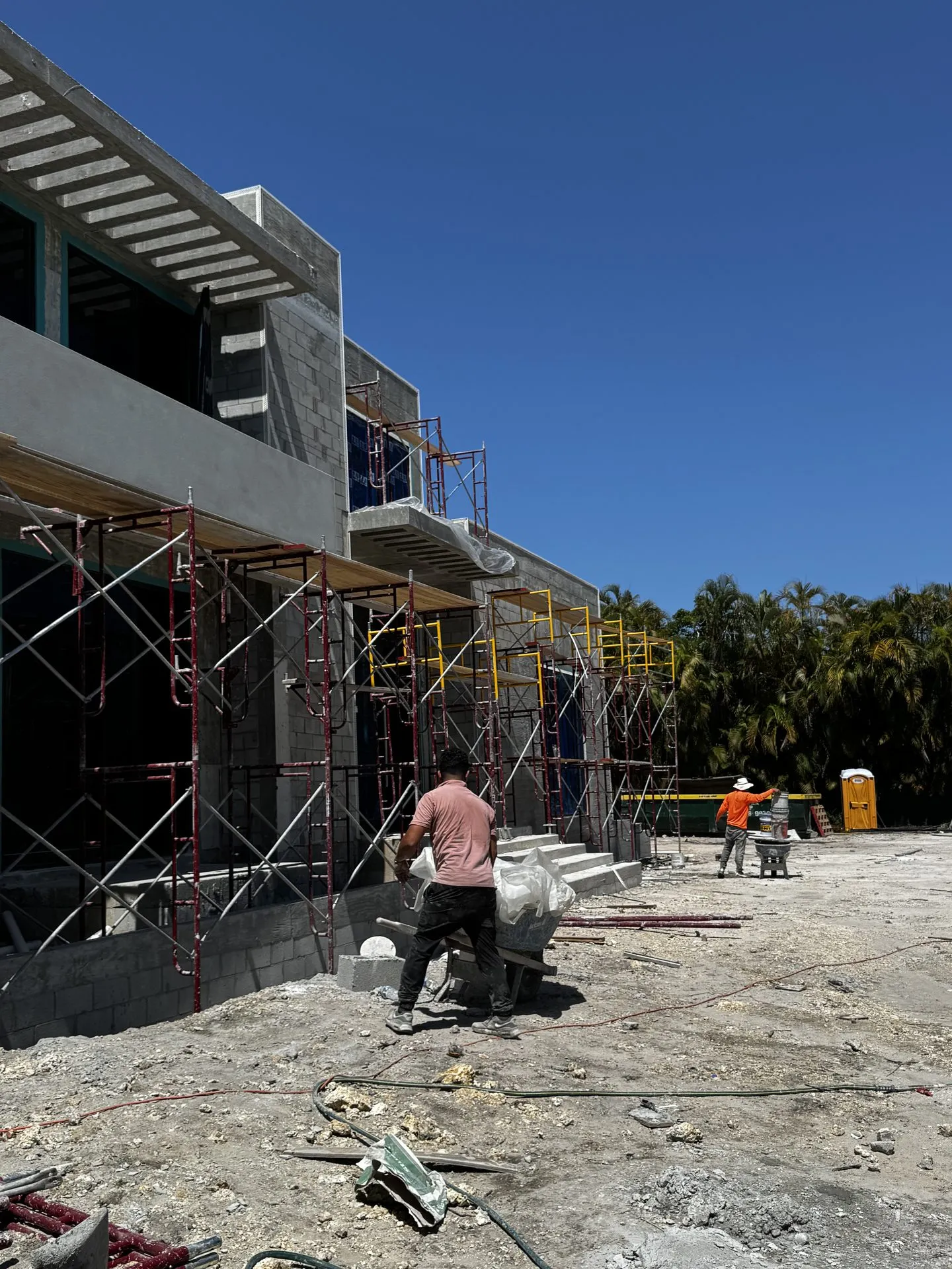 Worker moving material past a block building with scaffolding and balconies