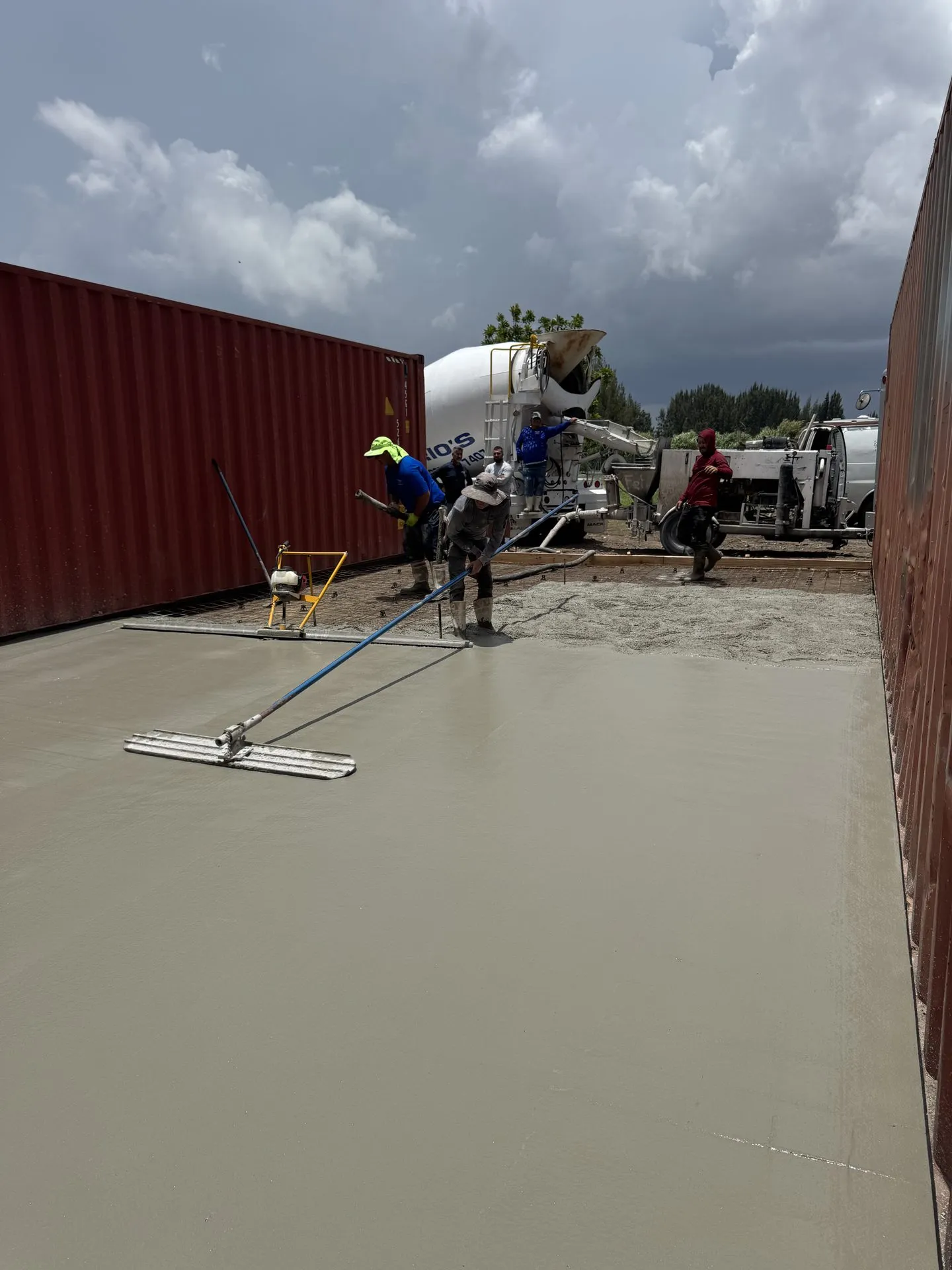 Concrete crew finishing a large slab with a power trowel next to a cement truck