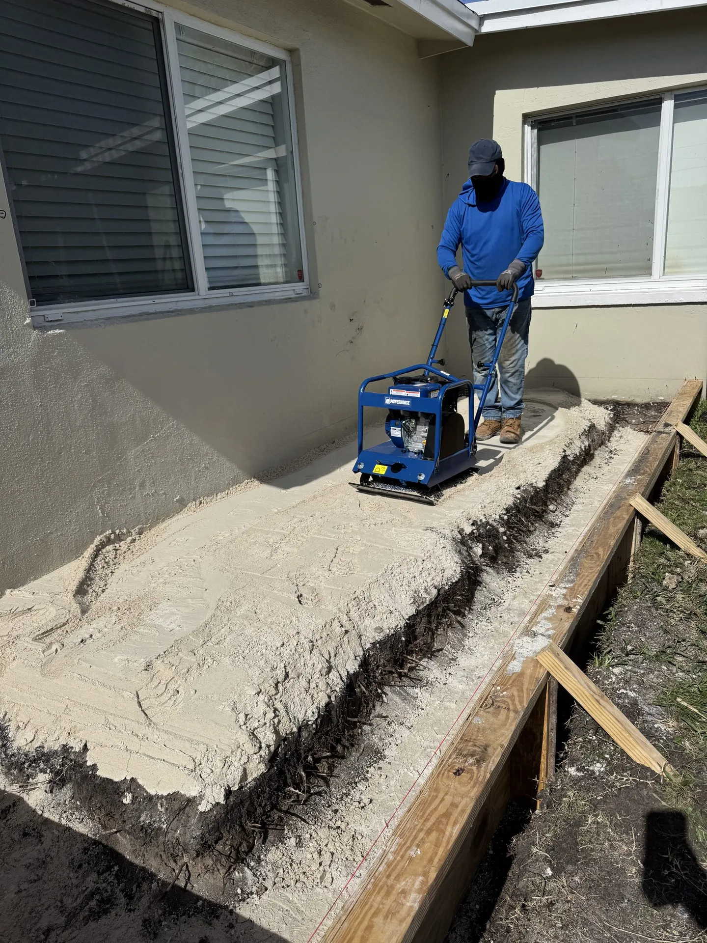 Worker compacting the base with a plate compactor before pouring concrete